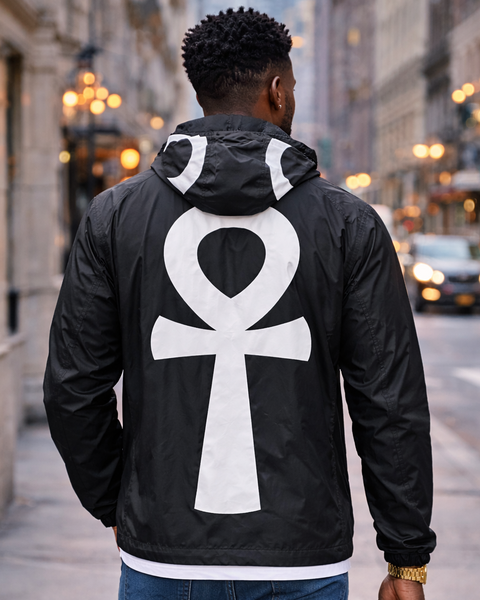 Person wearing a black jacket with a white ANKH symbol on the back, walking down a city street.