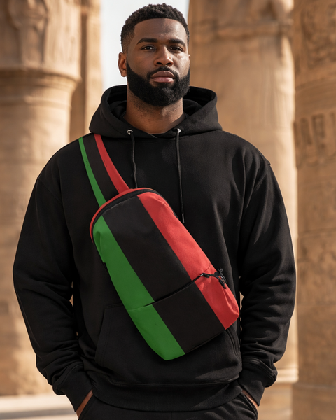 Man wearing a black hoodie with a red and green bag, standing in front of stone columns.
