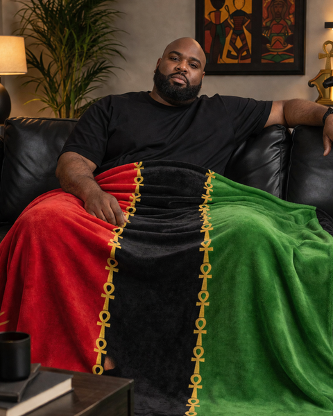 Man sitting on a couch with a colorful blanket draped over his lap in a living room setting.
